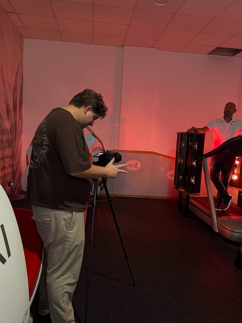 Ferdinando dietro una fotocamera su treppiede mentre riprende un cliente su un tapis roulant